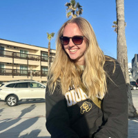 Corrina Schell smiles at the camera. Palm trees and a building are in the background