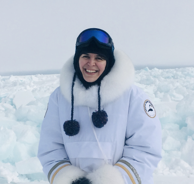 Tash stands outside in front of a scene of snow-covered sea ice in the Arctic