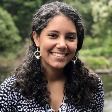 Melisa Diaz smiles at the camera in front of a scene filled with foliage