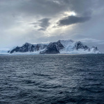 Sun behind the clouds, a few mountain peaks and ocean in the foreground