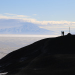 a mountain/volcano in the background, with a silhouette of a hill and two people in the foreground