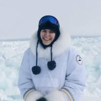 Tash stands outside in front of a scene of snow-covered sea ice in the Arctic