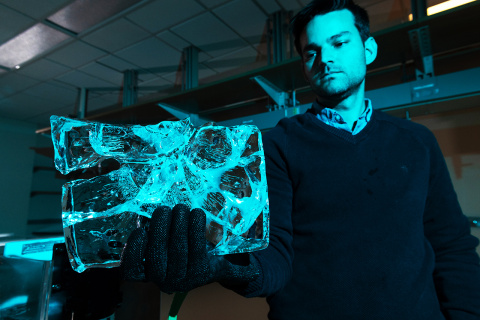 A man holding a piece of ice is pictured with blue lighting illuminating the frame and the right side of his body. 