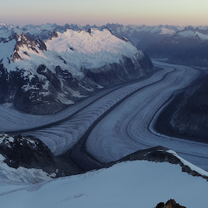Sun is rising on the horizon of an ice-covered mountain. 
