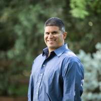 Person in a blue long-sleeved button-up shirt with blurred trees in the background.