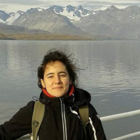 Maria Luisa (Marisa) stands outside on a boat in front of a backdrop of mountains