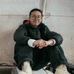 Aaron poses in fieldwork gear in a white-walled building 