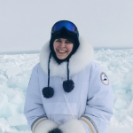 Tash stands outside in front of a scene of snow-covered sea ice in the Arctic