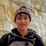 Ethan Sanchez at Zion national park. Ethan is smiling at the camera with shimmering rock behind him. 